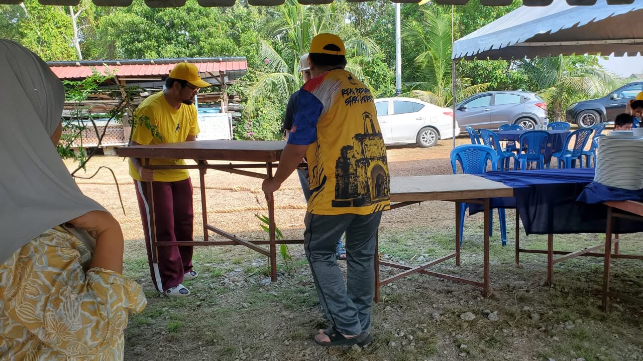 Aman Akil dan seorang peserta bekerjasama mengangkat meja di kawasan kenduri.