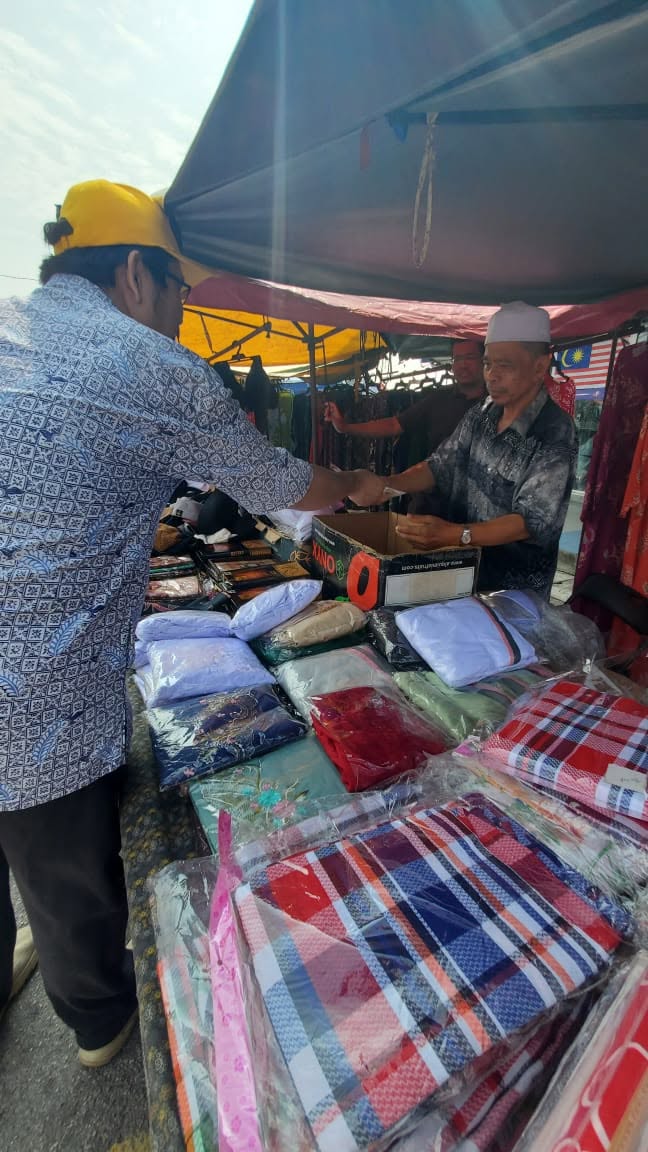 Aman Akil menyampaikan risalah kepada peniaga di sebuah gerai berbumbung kanopi.