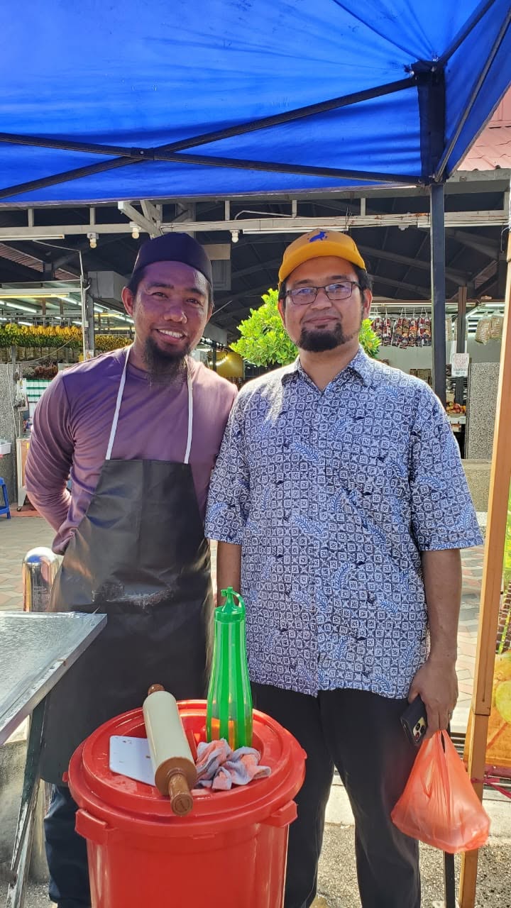 Aman Akil bergambar bersama seorang peniaga di bawah kanopi biru.