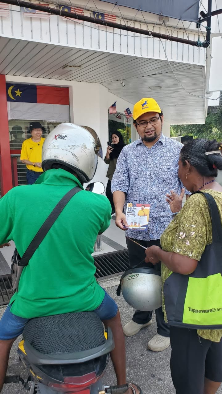 Aman Akil berbual dengan warga setempat berhampiran sebuah motosikal.