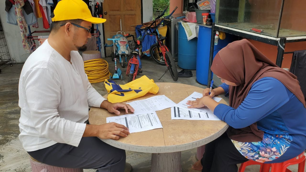 Aman Akil duduk bersama penghuni rumah yang sedang melengkapkan borang.