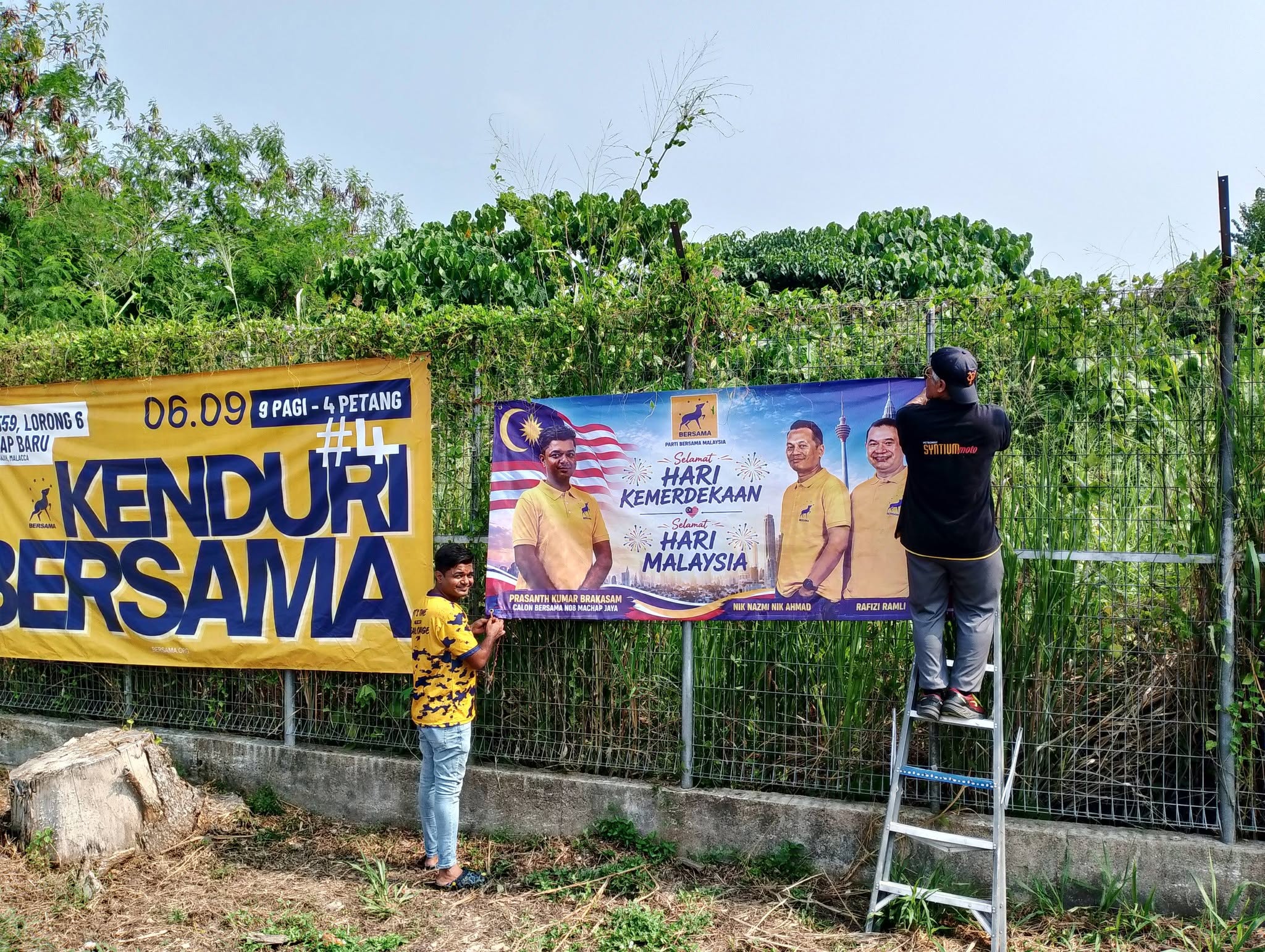Ahli pasukan memasang sepanduk Kenduri BERSAMA dan sambutan kebangsaan pada pagar.